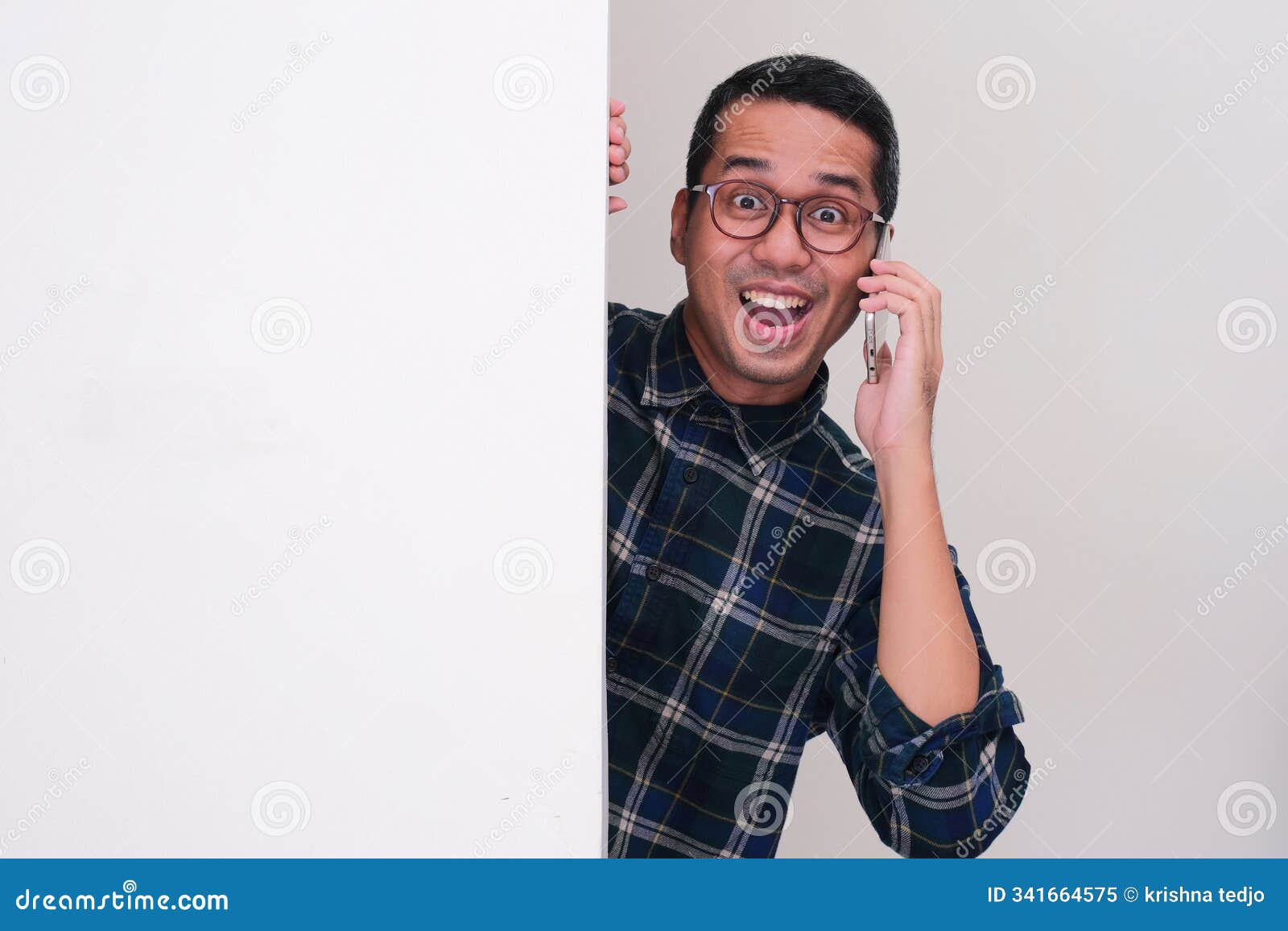 a man peeking from behind blank billboard showing excited face while calling