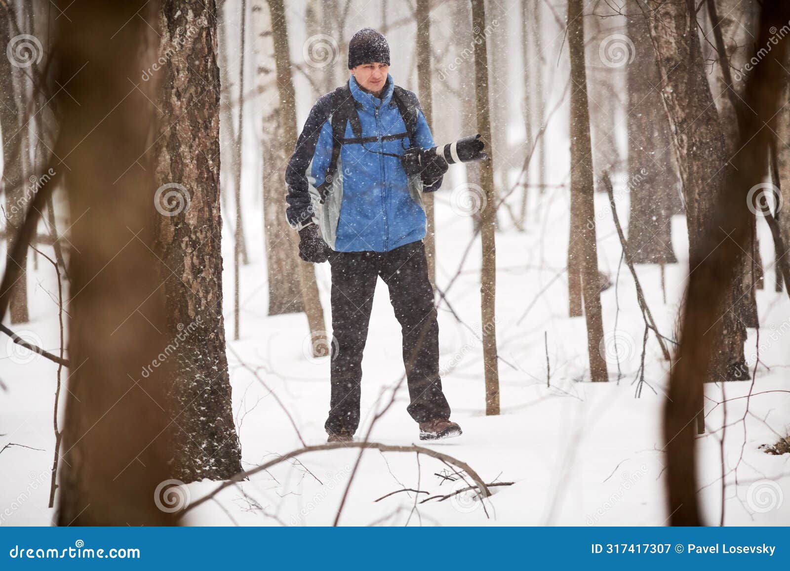 man with photocamera in forest during snowfall on