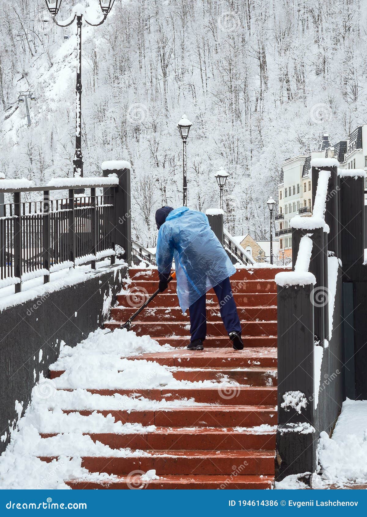 A Man in a Plastic Raincoat Removes Snow on the Steps Against the