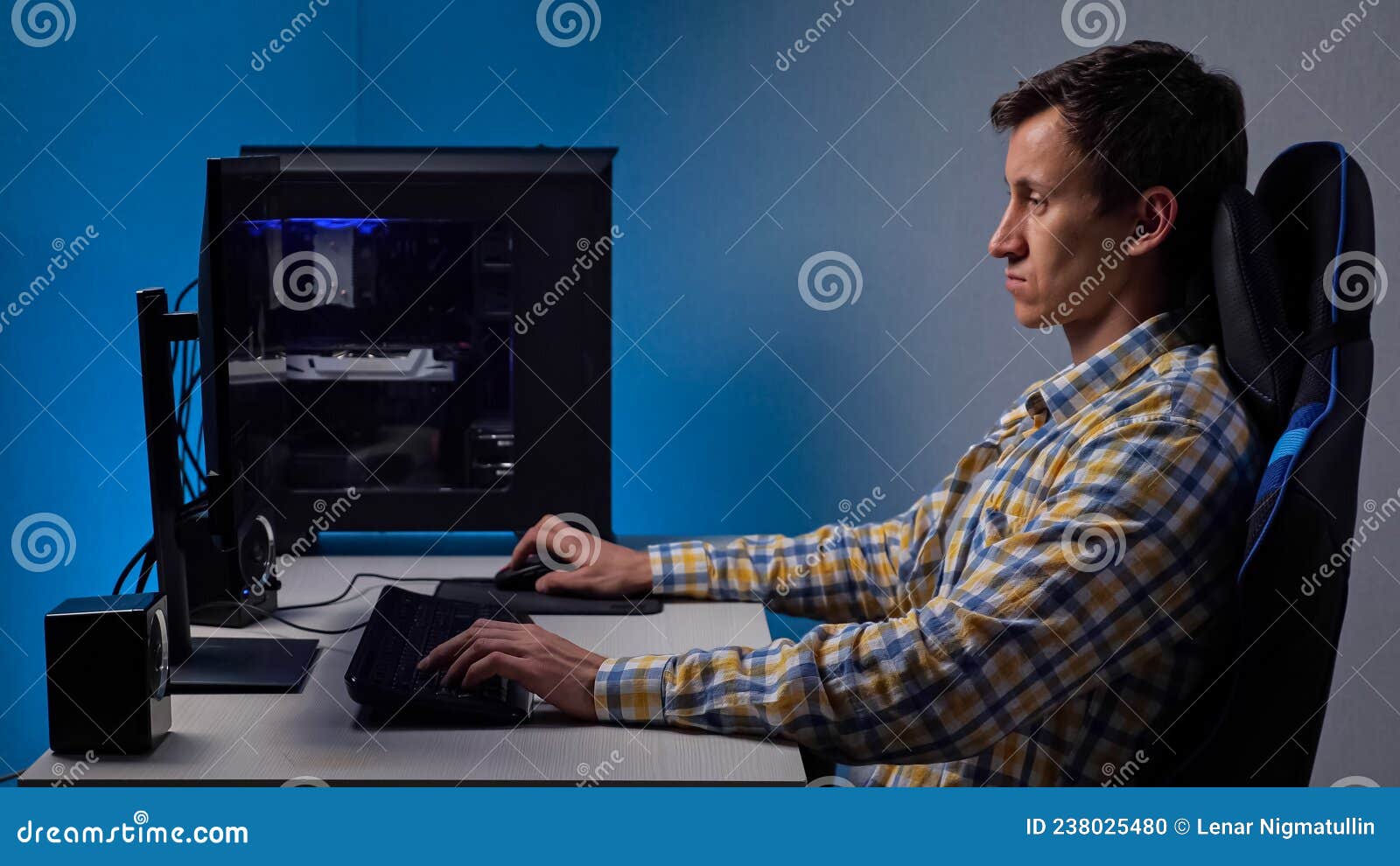 man plays videogame on large computer screen sitting in gaming chair in semi-dark room illuminated by monitor.