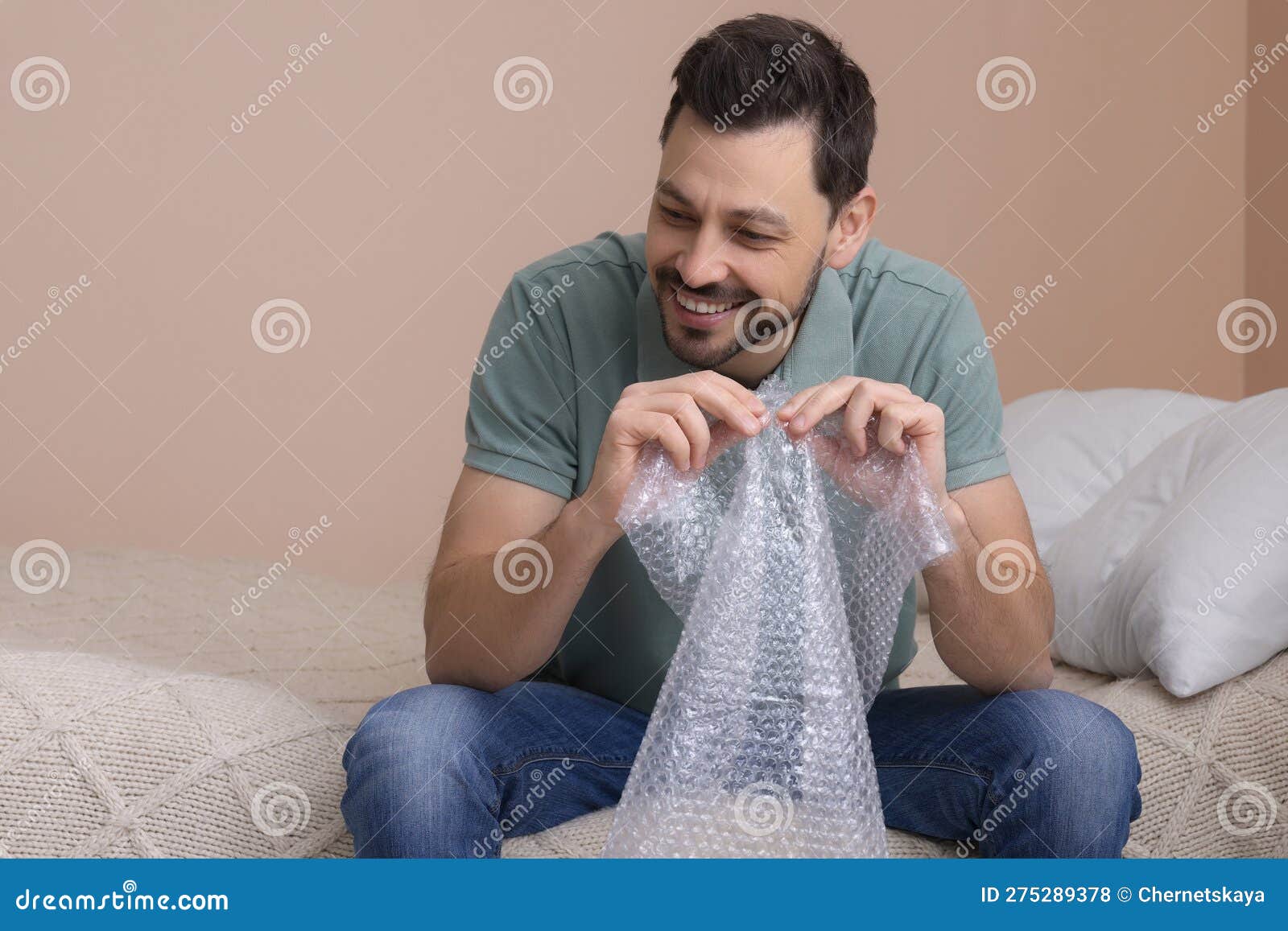Man Popping Bubble Wrap in Bedroom at Home. Stress Relief Stock Photo