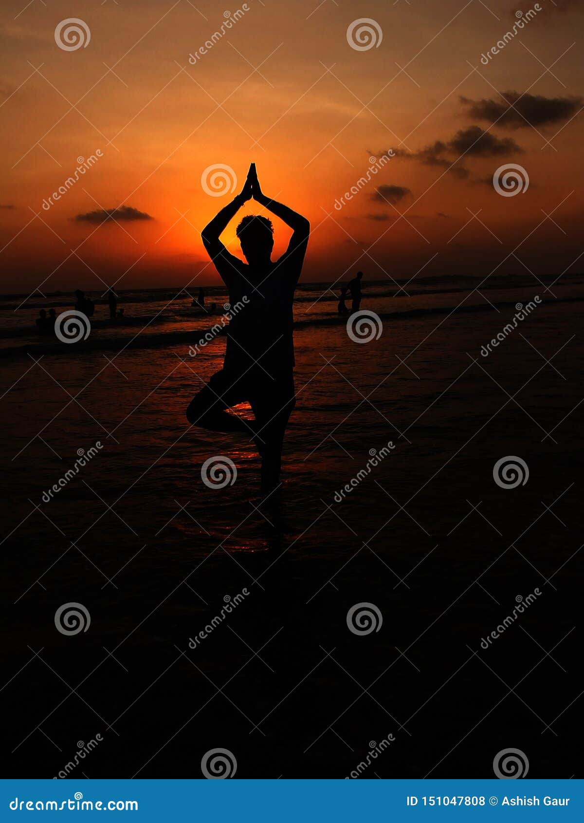 man posing in vriksha asana yoga pose on the sea beach during sunrise
