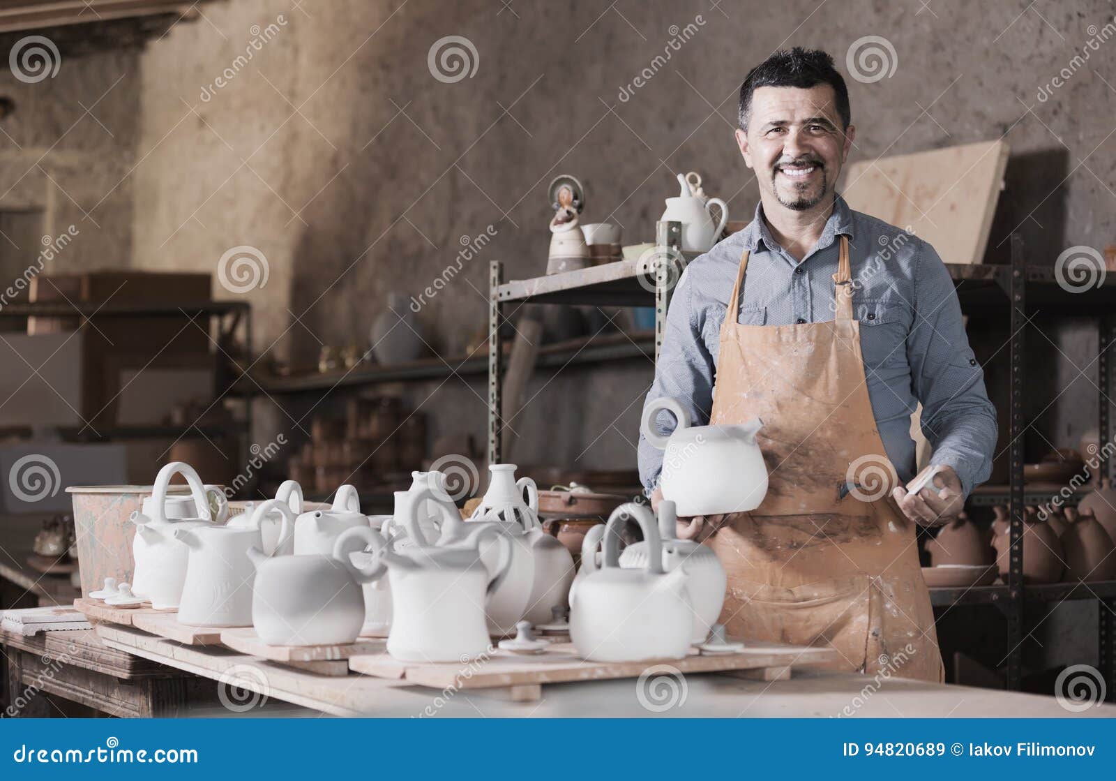 Positive man potter holding ceramic vessels in atelier