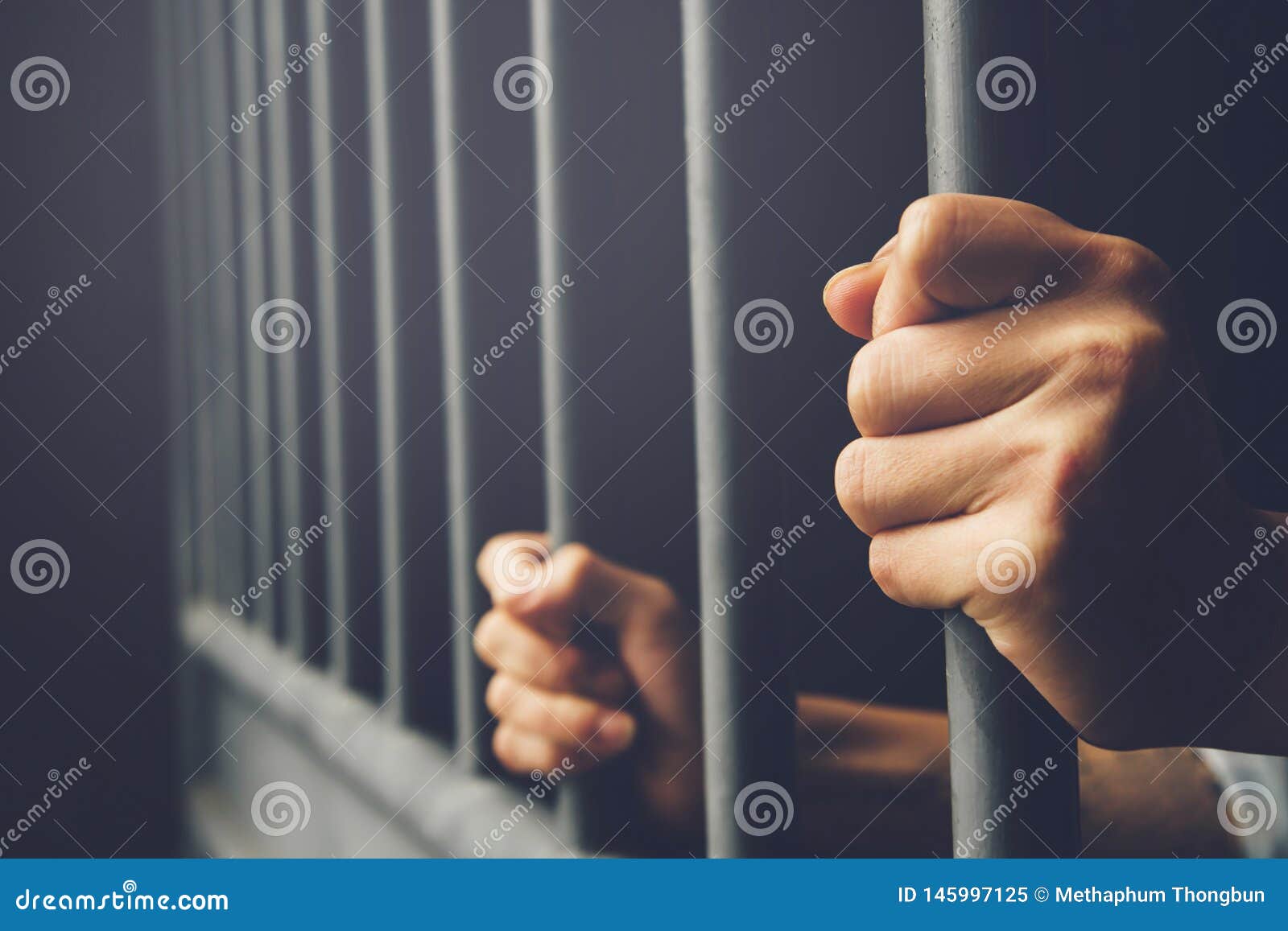 man in prison hands of behind hold steel cage jail bars.