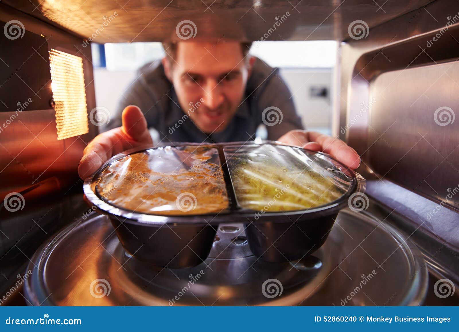 man putting tv dinner into microwave oven to cook