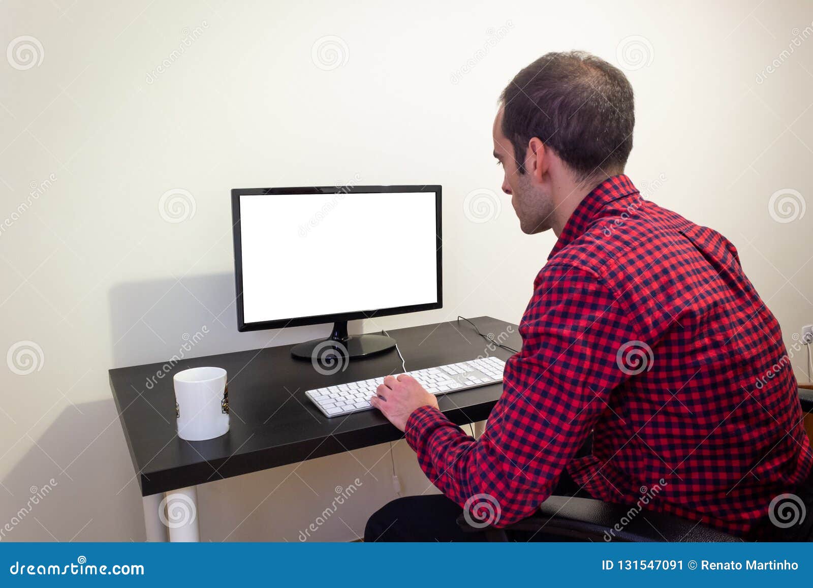 Man på kontorsdatoren på träsvart skrivbordmodell Prickig röd skjorta, LCD-skärm, tangentbord, mus, skrivbords- dator, kontorssto. Man på kontorsdatoren på träsvart skrivbordmodell Den prickiga röda skjortan, LCD-skärmen, tangentbordet, musen, den skrivbords- datoren, kontorsstol som är vit rånar tillbaka sikt kopiera avstånd