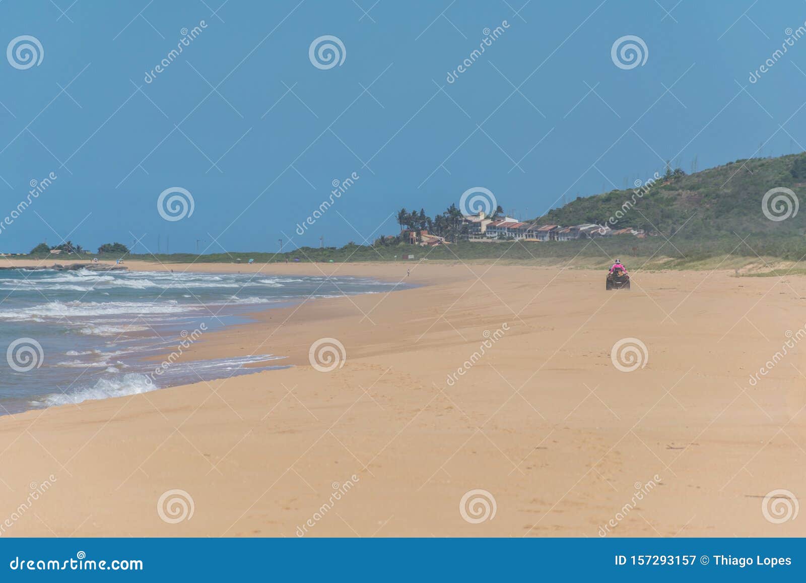 a man red-dressed is riding a quadricycle on the brazilian coast, a cluster of beach houses in a mountain foot, the