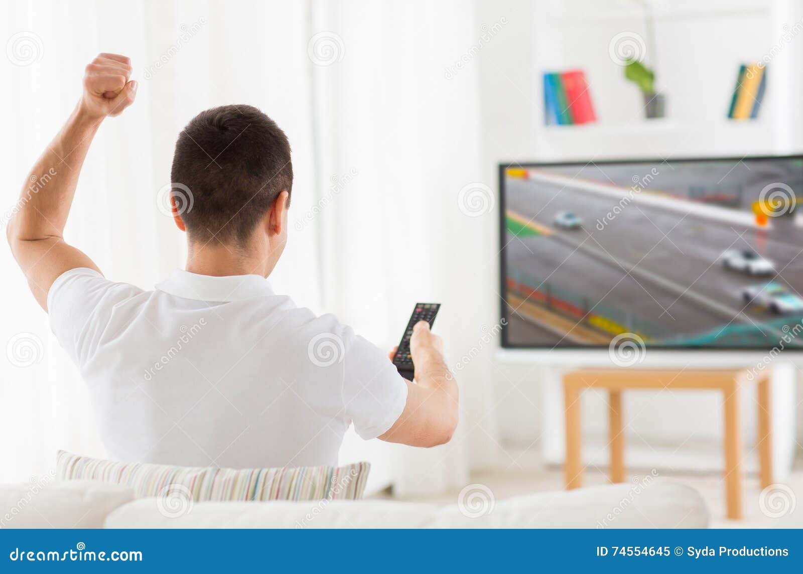 man with remote watching motorsports on tv at home