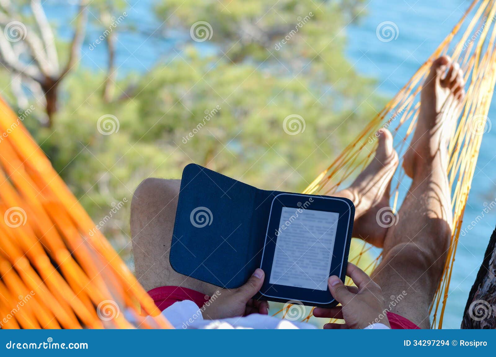 man resting in hammock on seashore and reading ebook