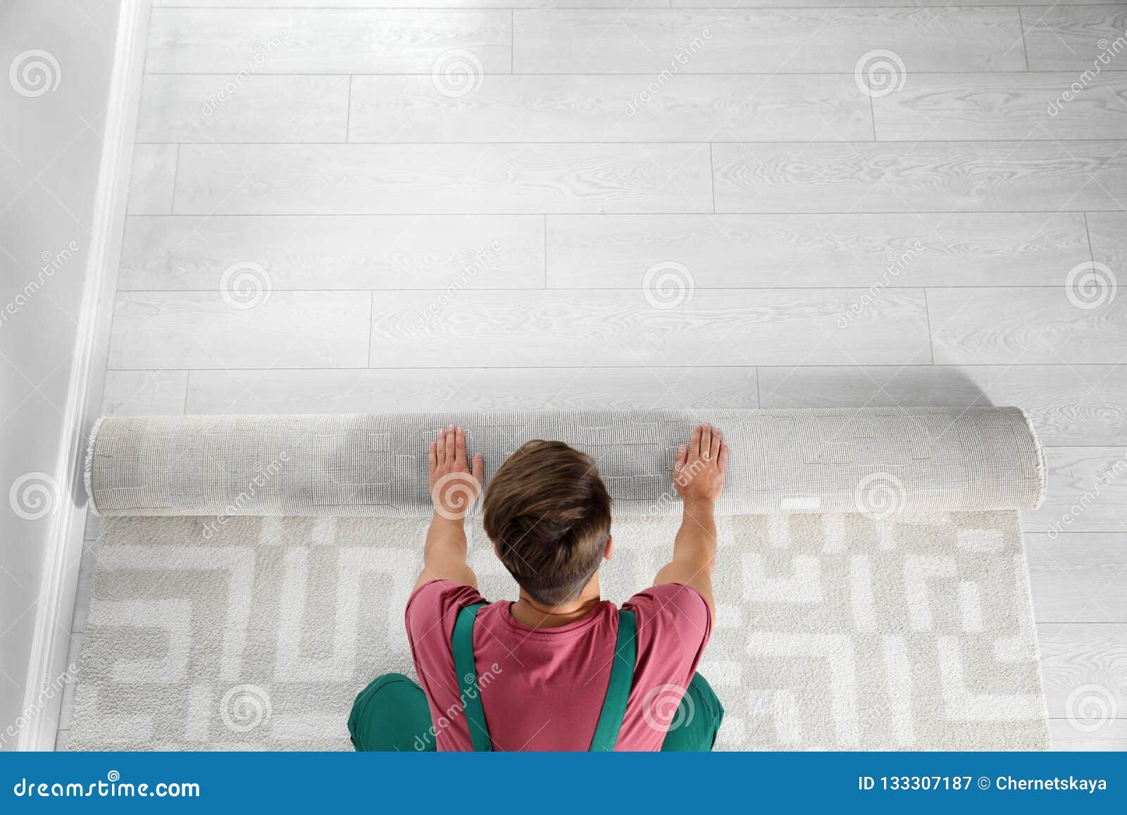 man rolling out new carpet flooring indoors, top view.