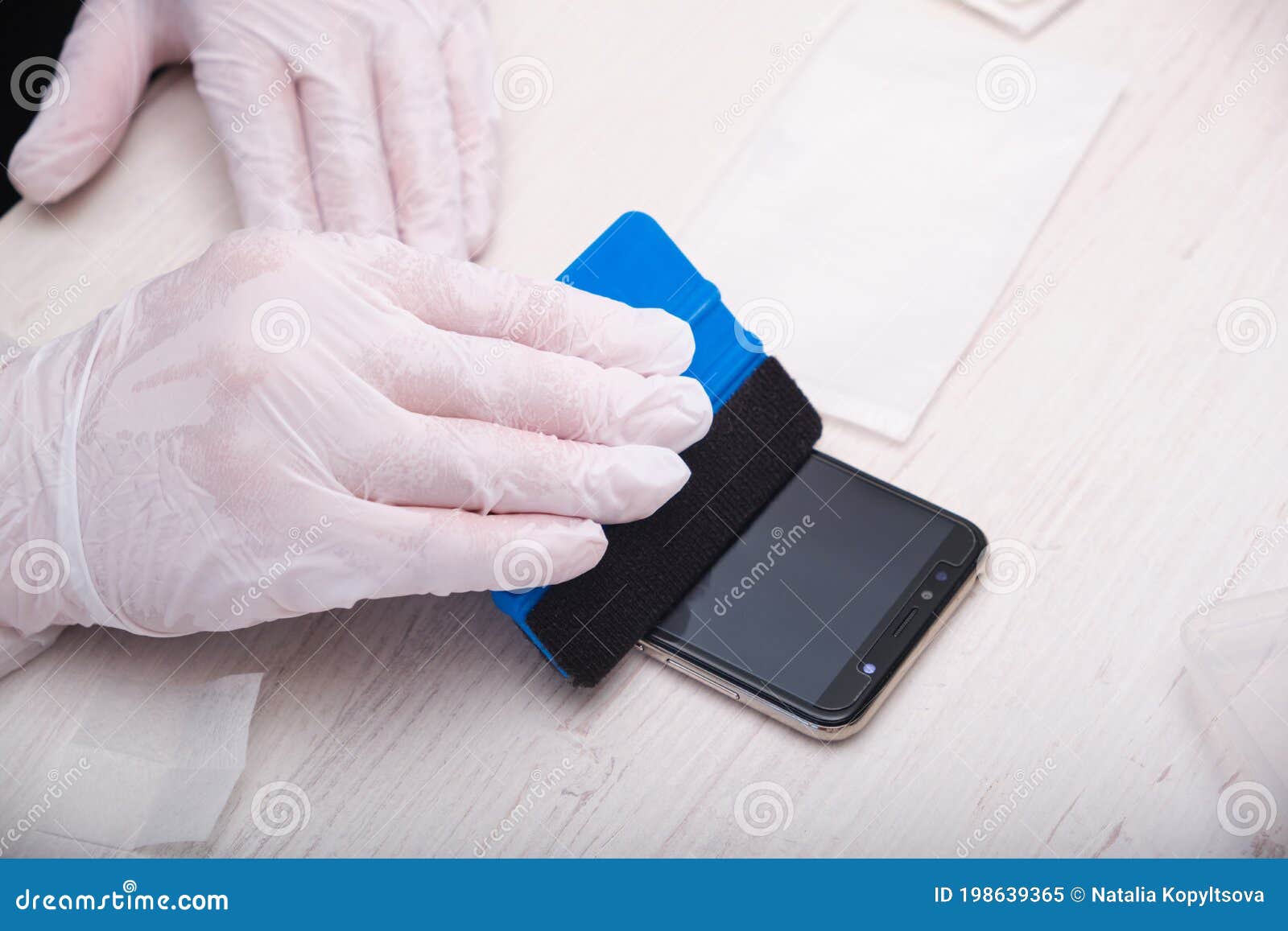 man in rubber gloves glues a protective glass to a smartphone using a special palstic spatula with a soft nozzle