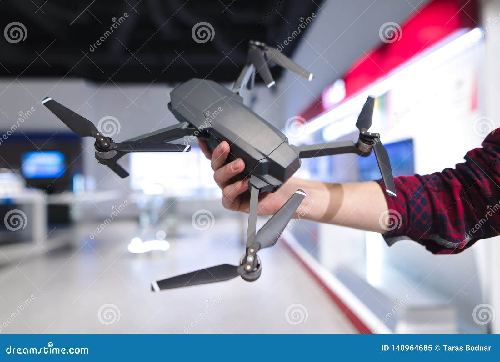 man`s hand holds a quadcopter in the background of a electronics store. purchase a dron in a hardware store