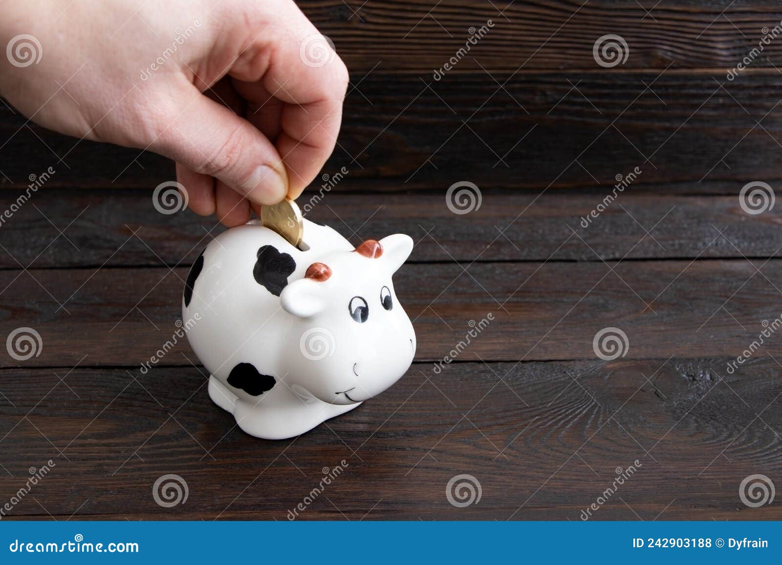 a man`s hand puts a coin in the piggy bank on a wooden background.saving money. family budget. money box on a wooden table.coin