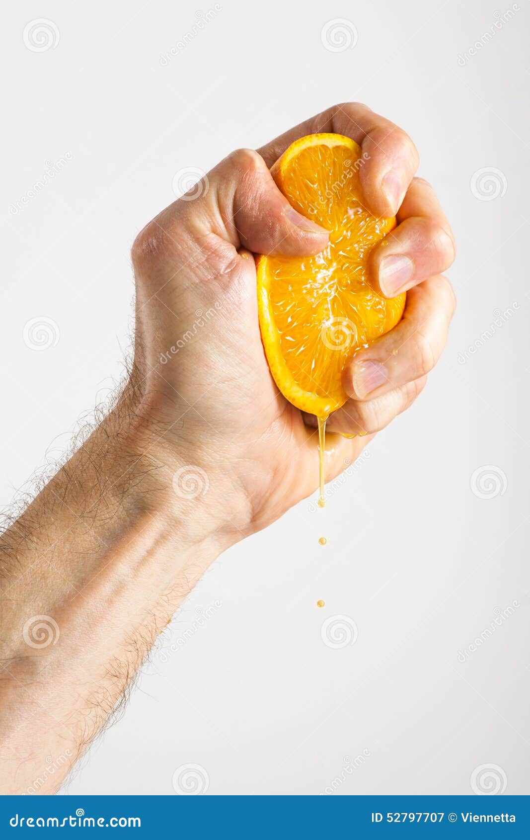 An anonymous man s hand squeezing an orange half until the juice comes out on a gray background.