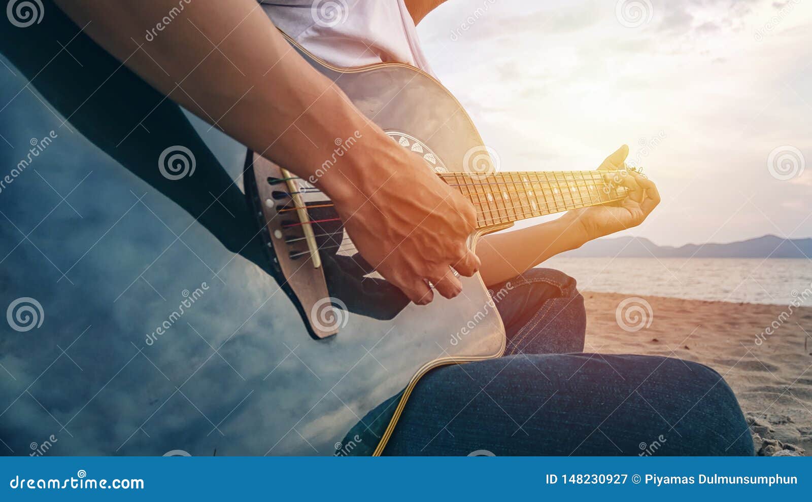 man`s hands playing acoustic guitar, capture chords by finger on sandy beach at sunset time. playing music concept