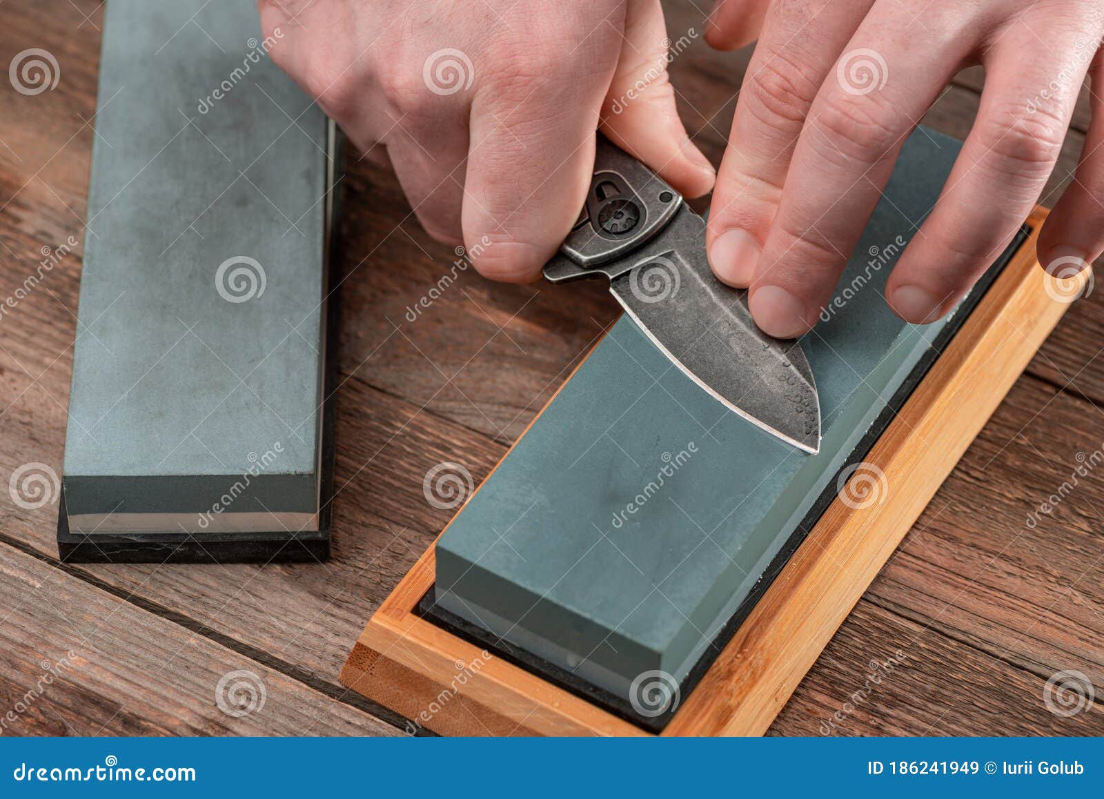 man sharpening a jackknife with a whetstone on wooden background