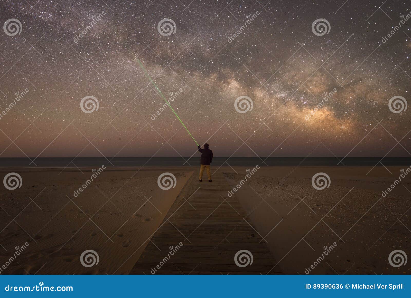 man shining green laser to point at a star in the sky