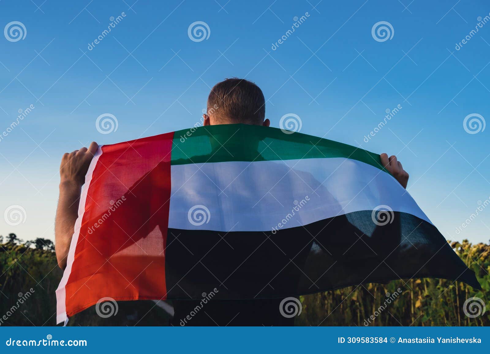 man showing national flag of uae waving in the wind during sunset. national independence day or flag day. flag of united