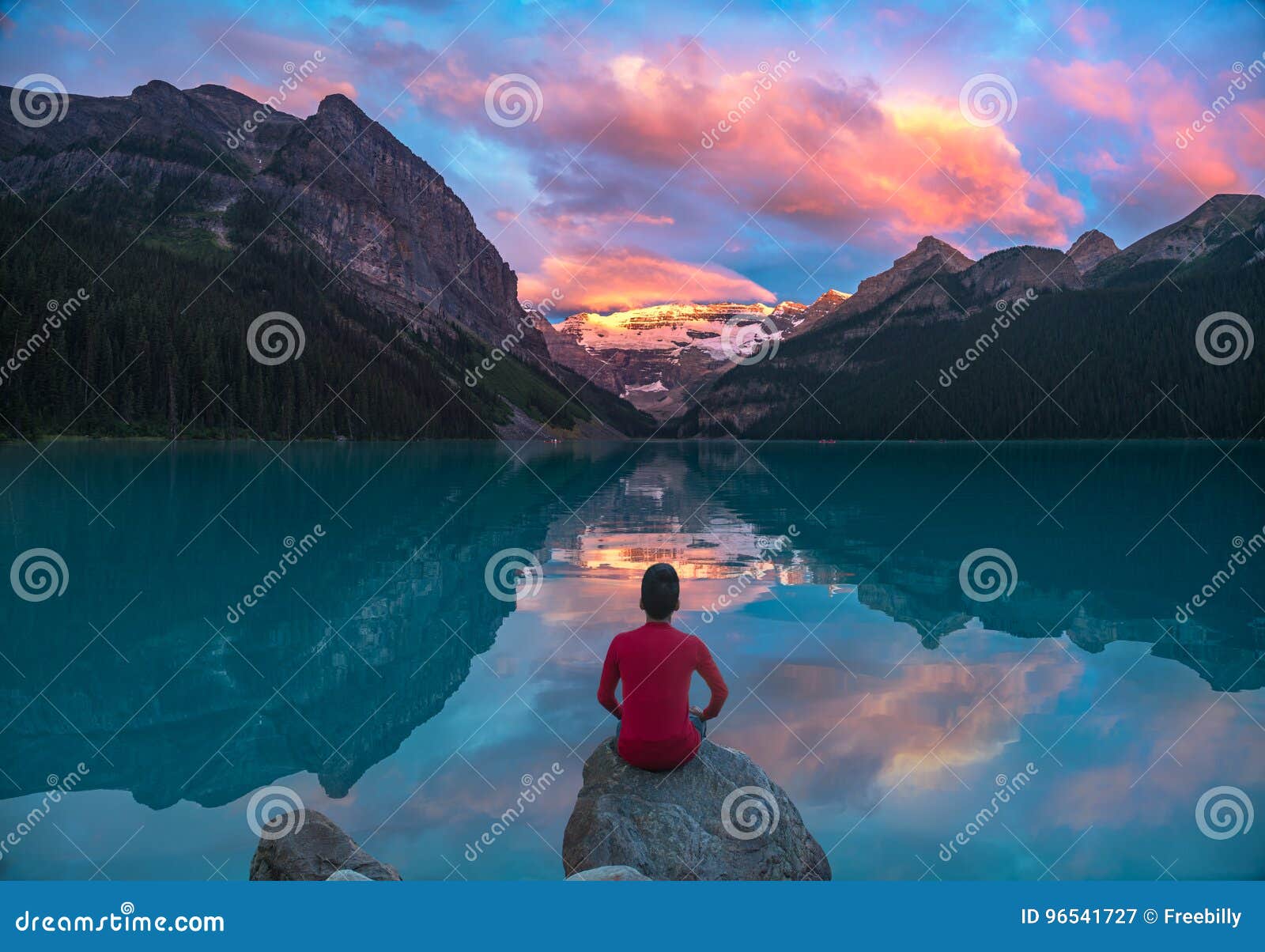 man sit on rock watching lake louise morning clouds with reflect