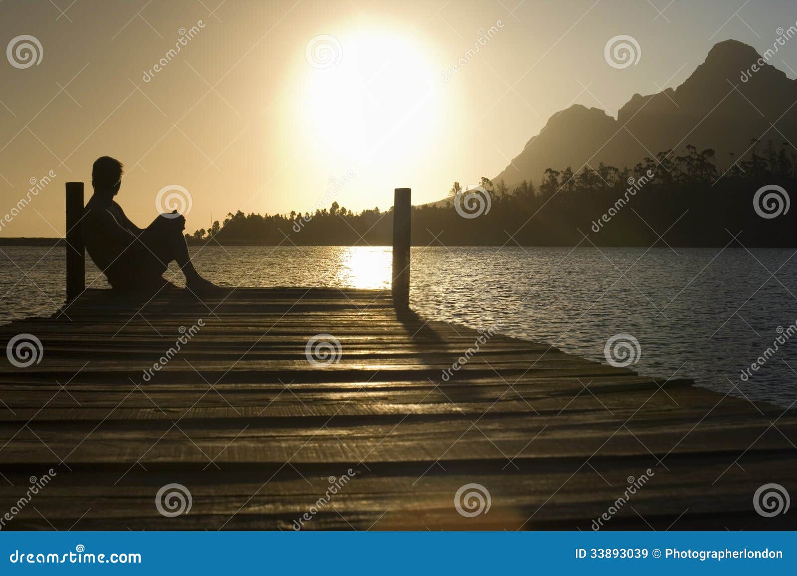 man sitting on dock by lake