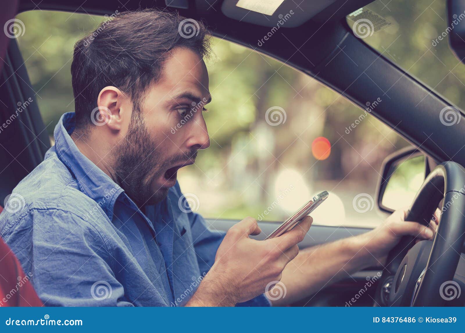 man sitting inside car with mobile phone texting while driving