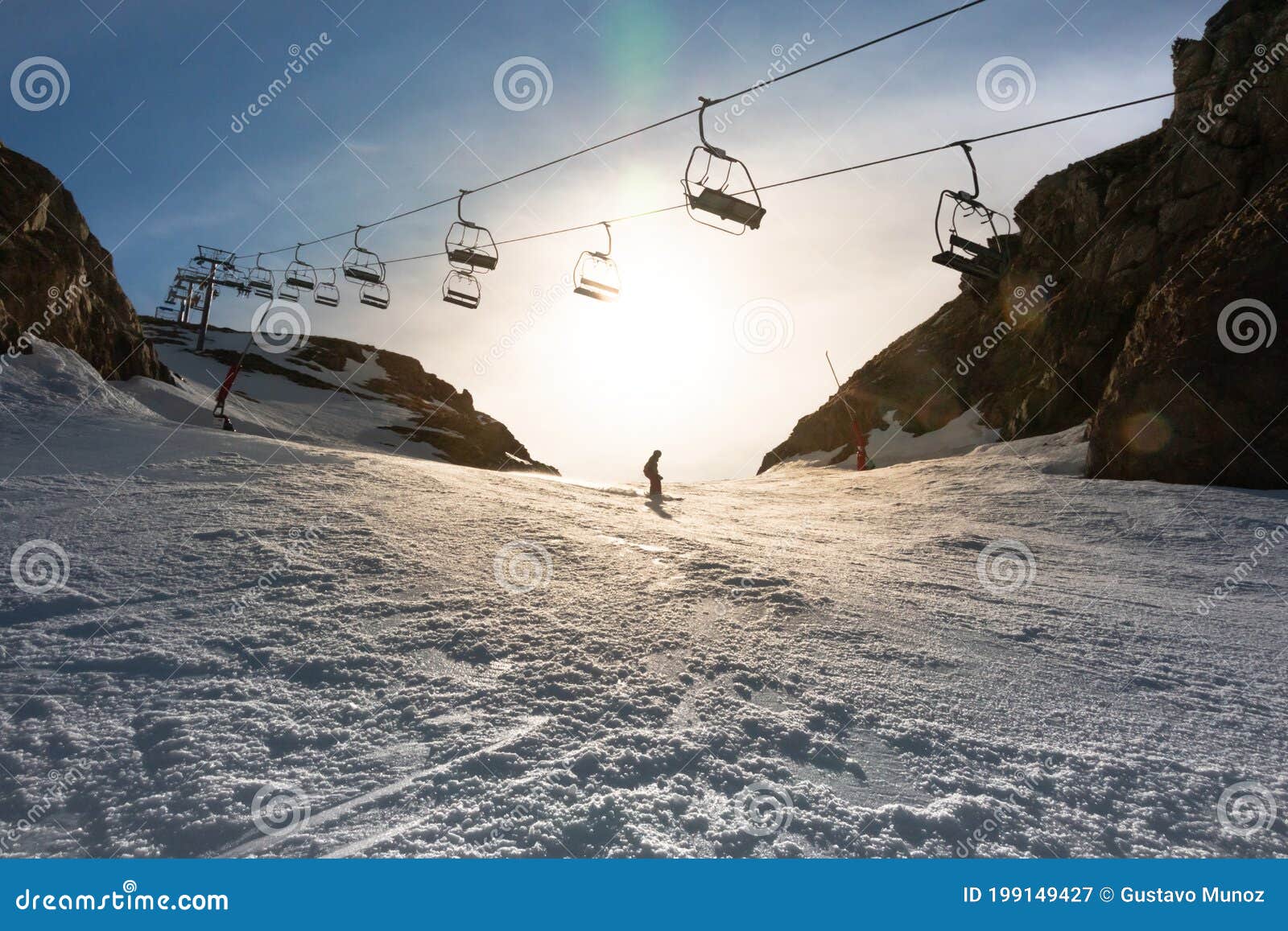 A Man Skiing Down a Slope Passing Under a Ski Lift in Backlit Stock