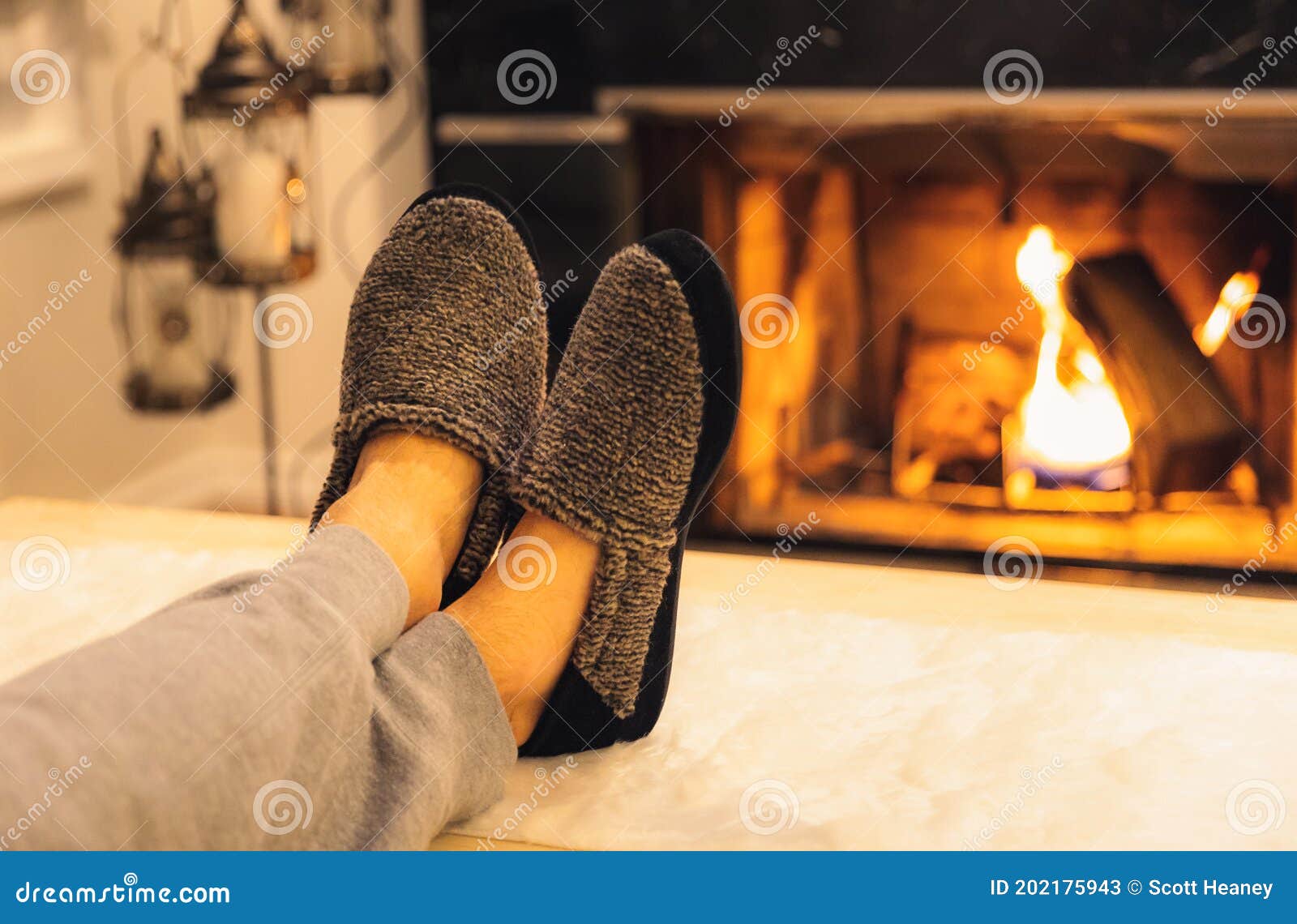 man in slippers relaxing with his feet up with a fireplace in the background.