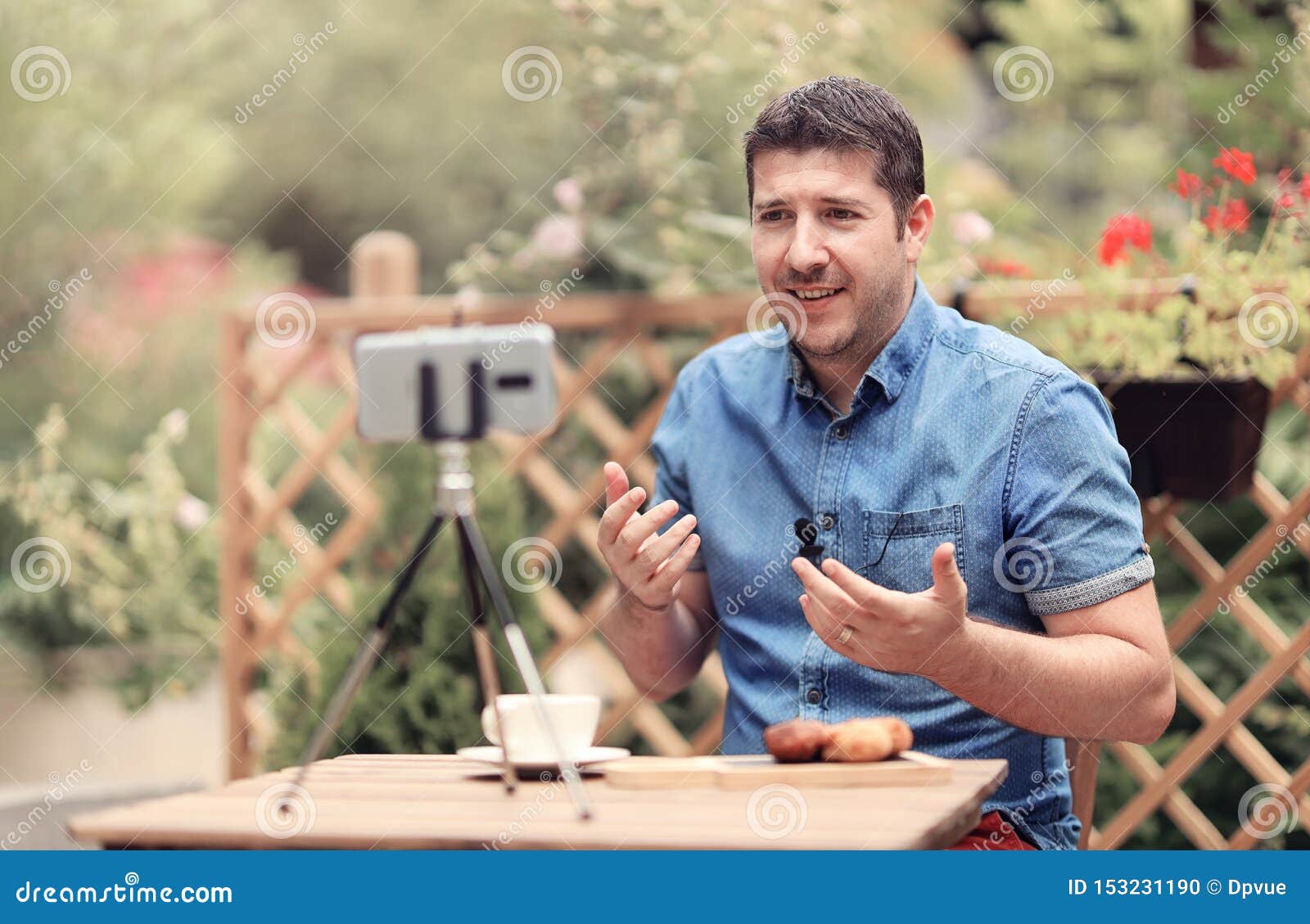 man speaking in front of camera with attached mic lavalier. vlogger man sitting on a table and making a vlog episode