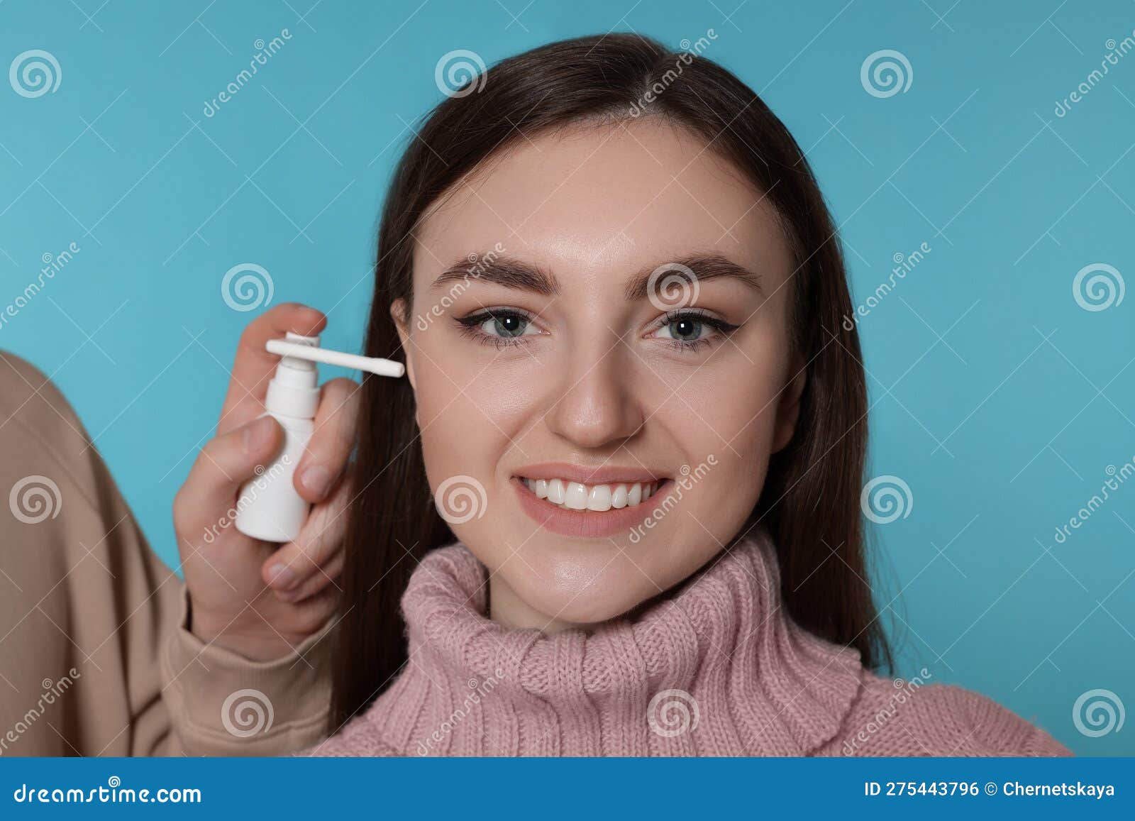 man spraying medication into woman`s ear on light blue background