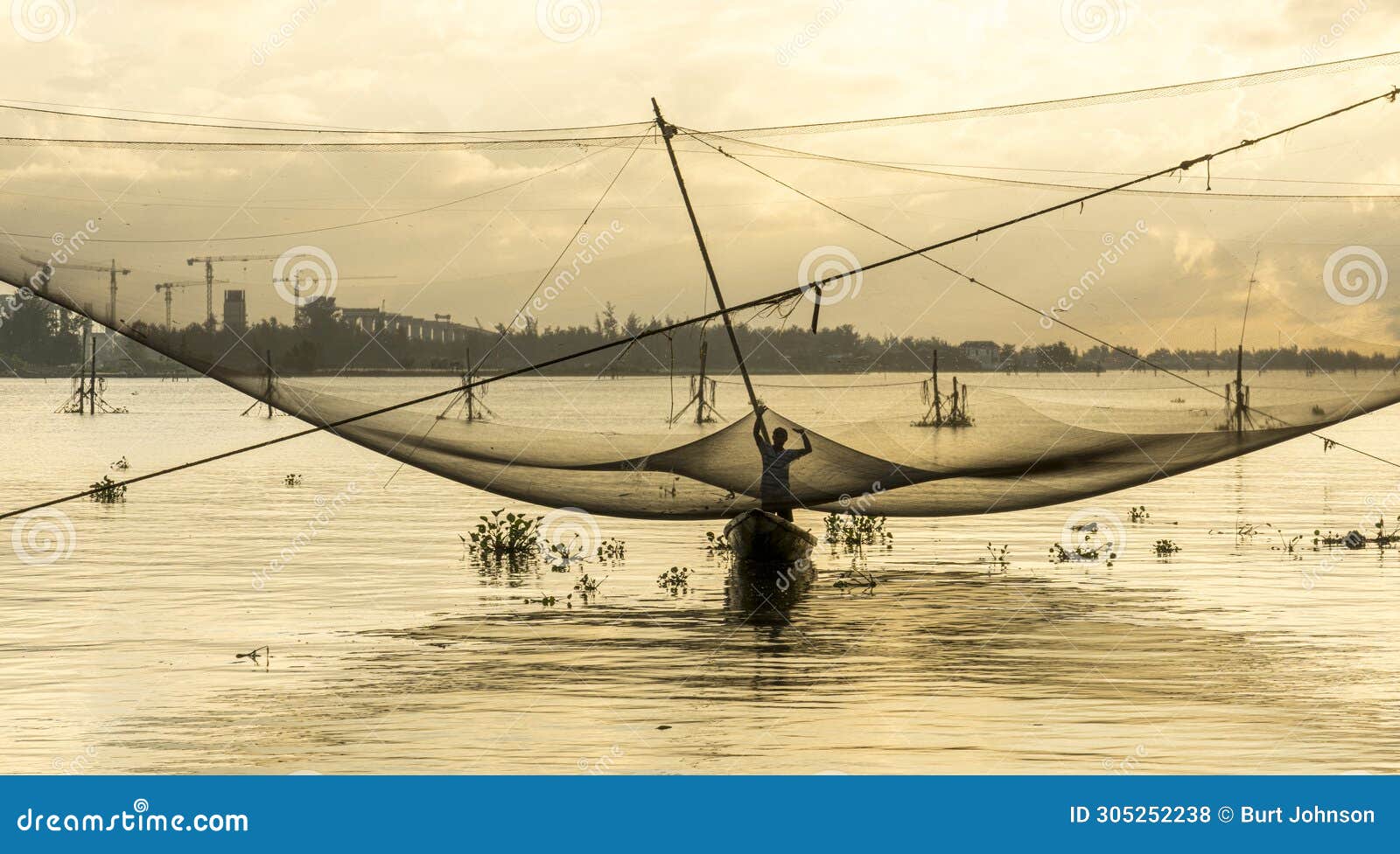 Man Standing in Boat on Water with Fishing Nets at Sunrise in Hoi