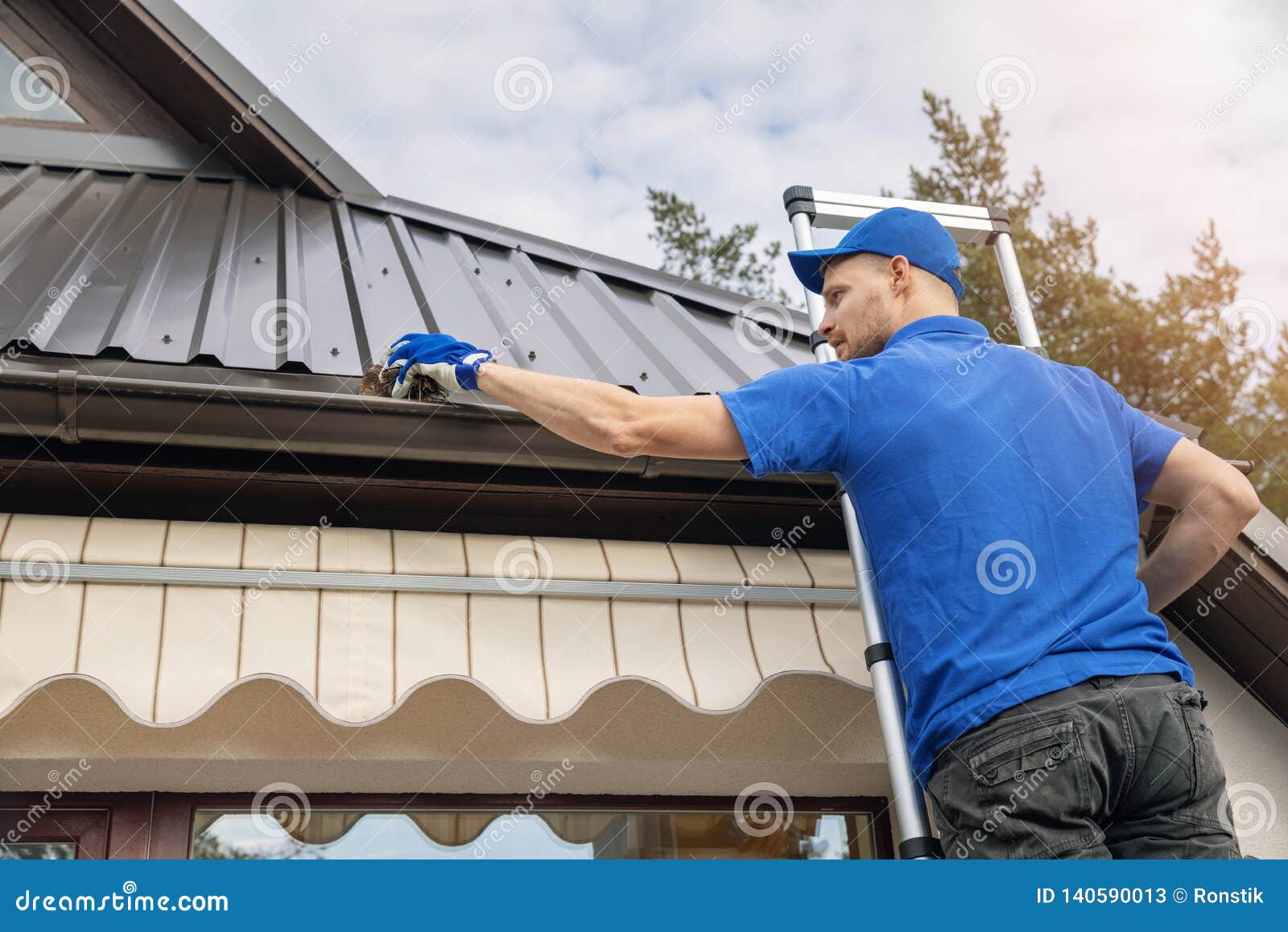 man standing on ladder and cleaning roof rain gutter