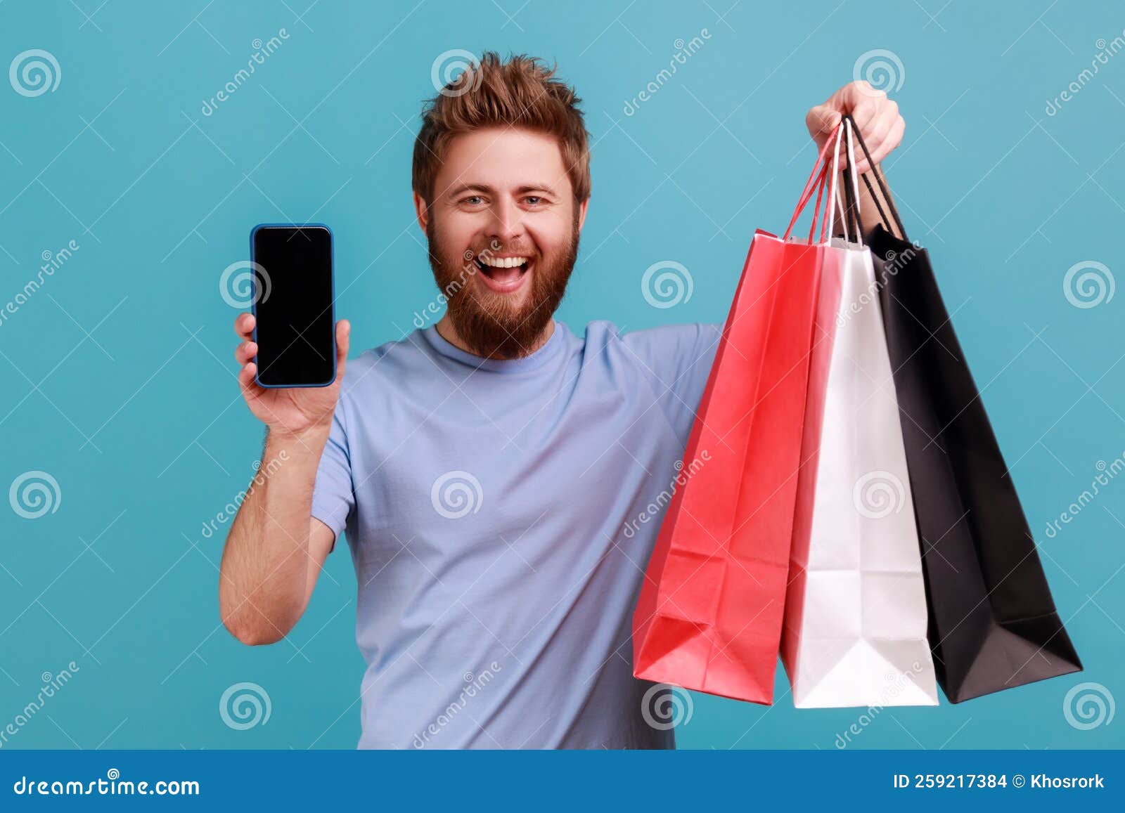 Man Standing With Satisfied Look Showing Shopping Bags And Smart Phone With Blank Screen Stock