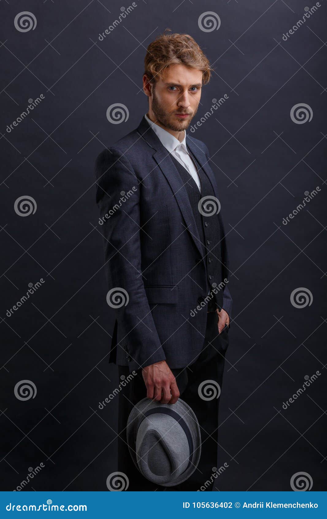 A Man in a Suit, Stands with a Serious Look and Holds a Hat in His ...