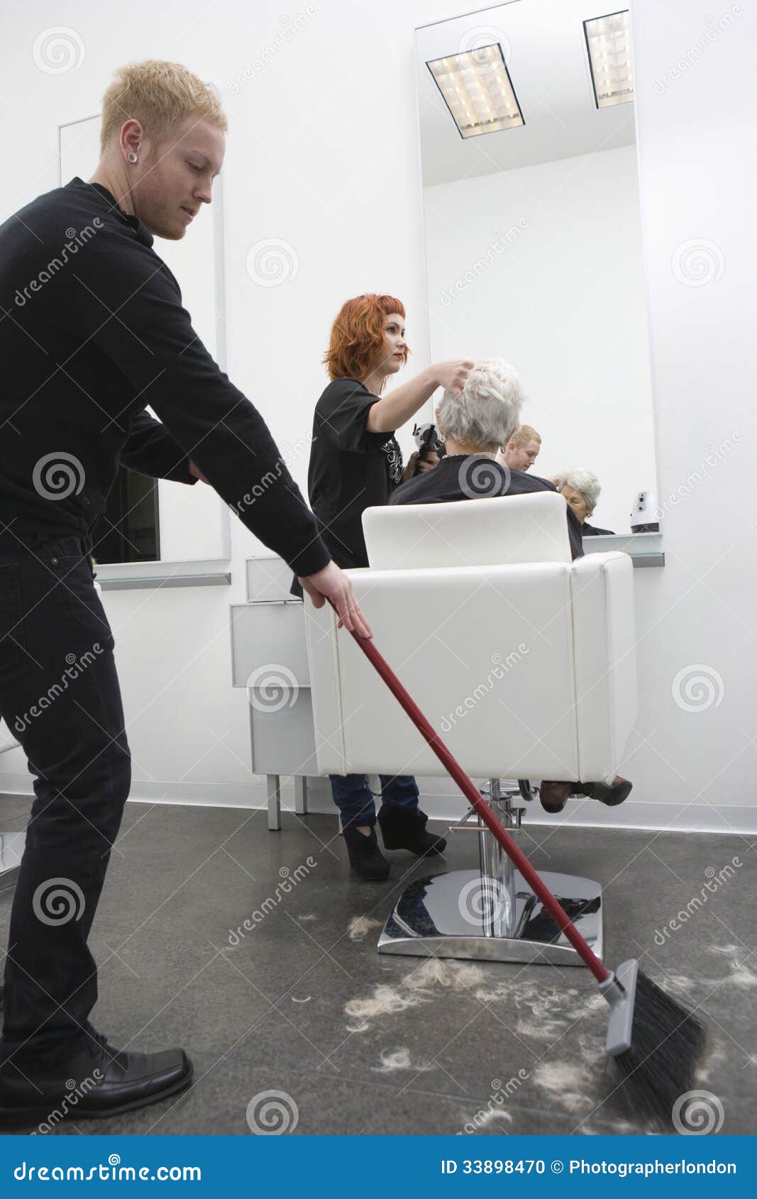 Man Sweeping While Hairdresser Giving Haircut To Senior Man Sweeping While Hairdresser Giving Haircut To Senior