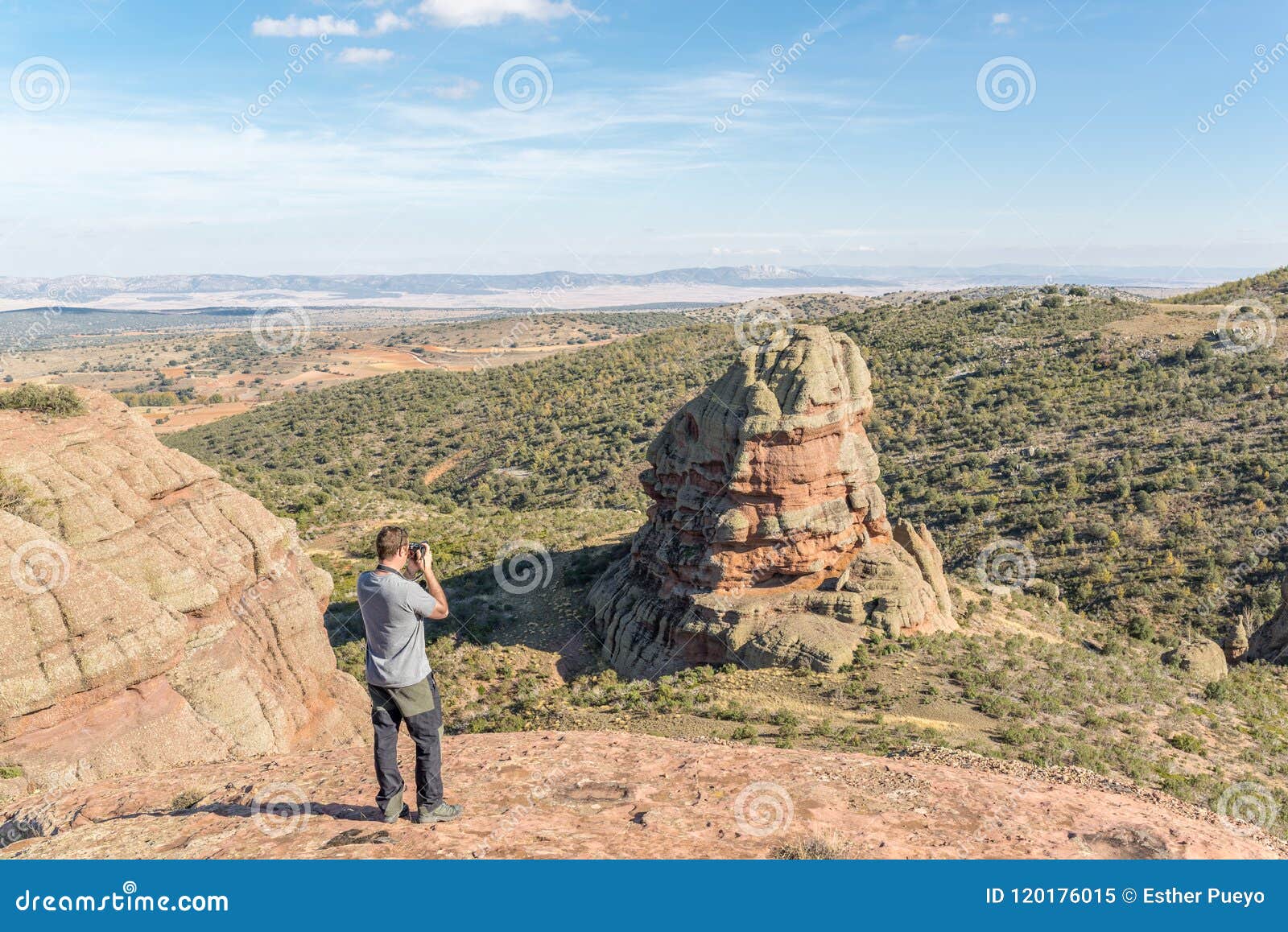 young man taking a photo of a rodeno boulder in perecens, teruel, spain.