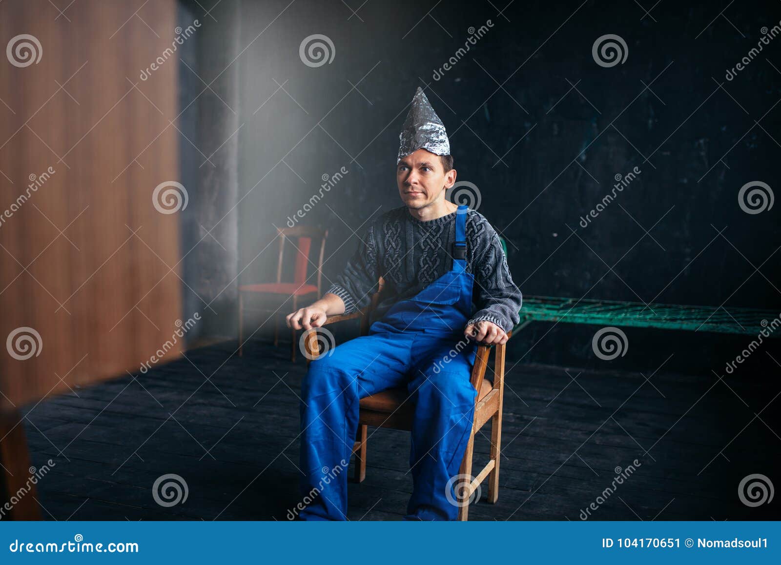 man in tinfoil hat sits in chair, paranoia concept