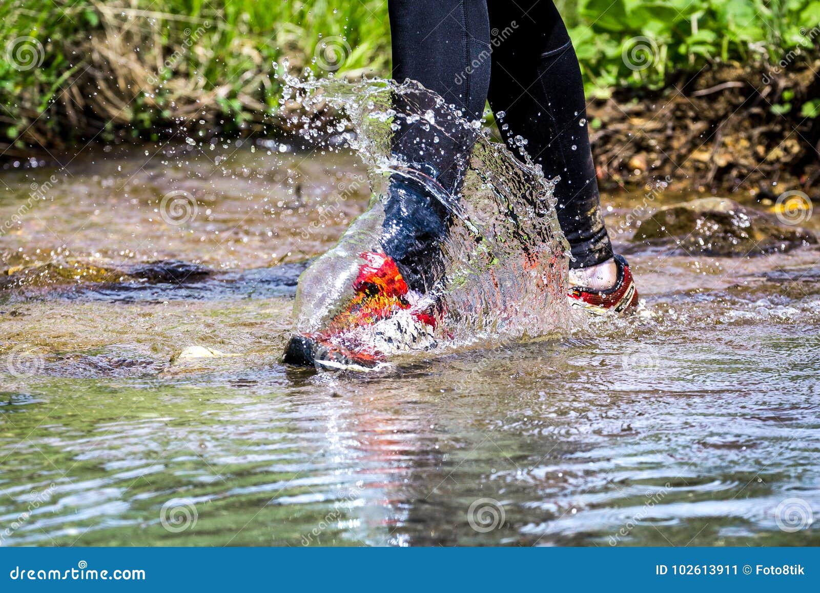 man trail running in the mountains, crossing a creek