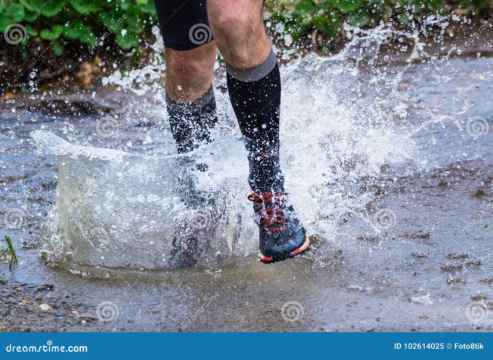 man trail running in the mountains, crossing a creek
