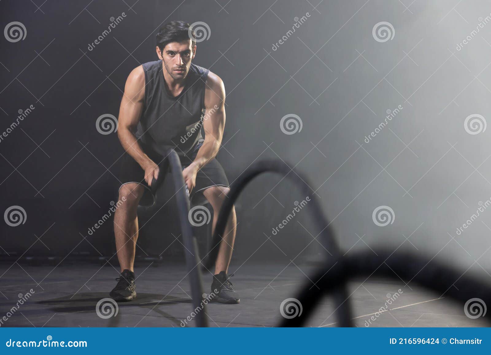 Man Using Battle Ropes for Whipping Exercise in a Gym Stock Photo