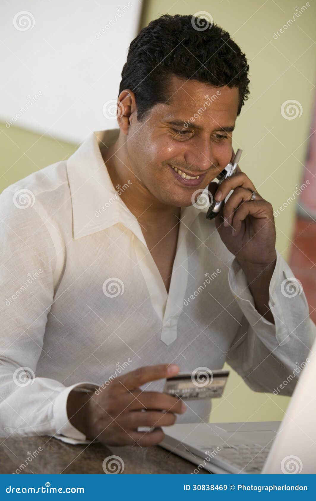 Man Using Cell Phone and Laptop To Purchase with Credit Card at Home