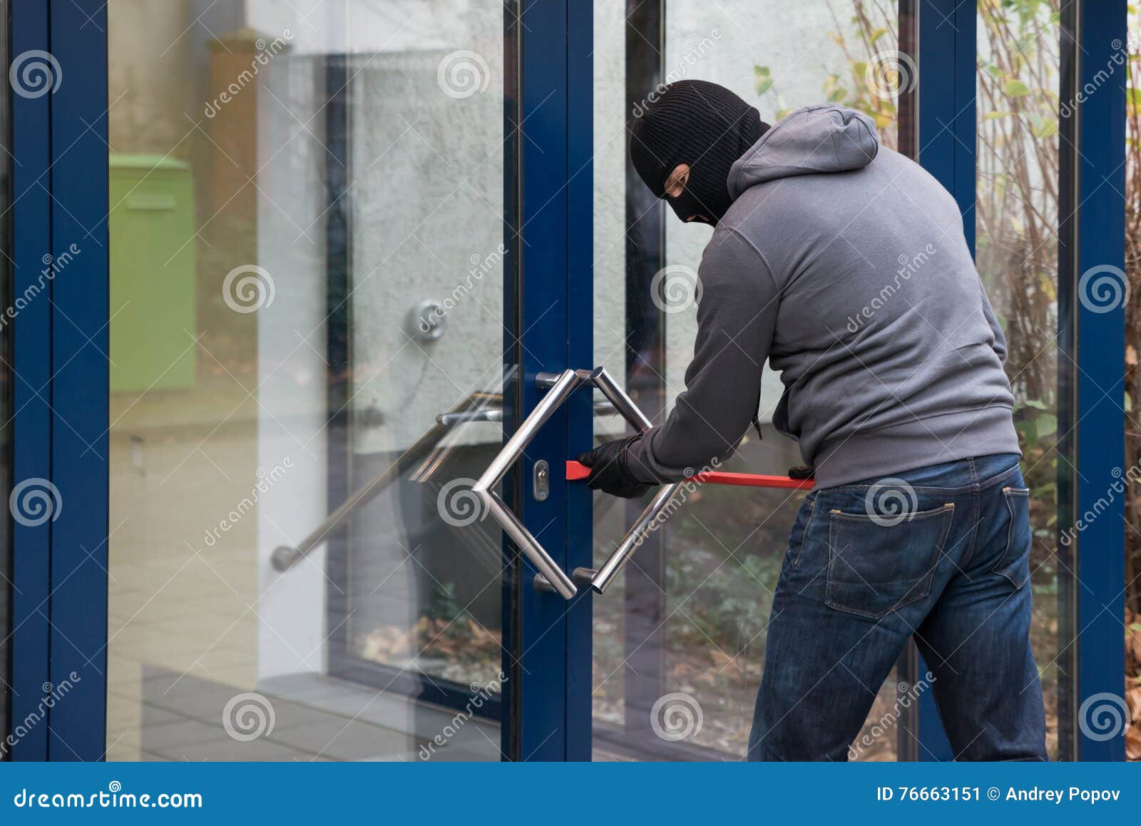 man using crowbar to open glass door