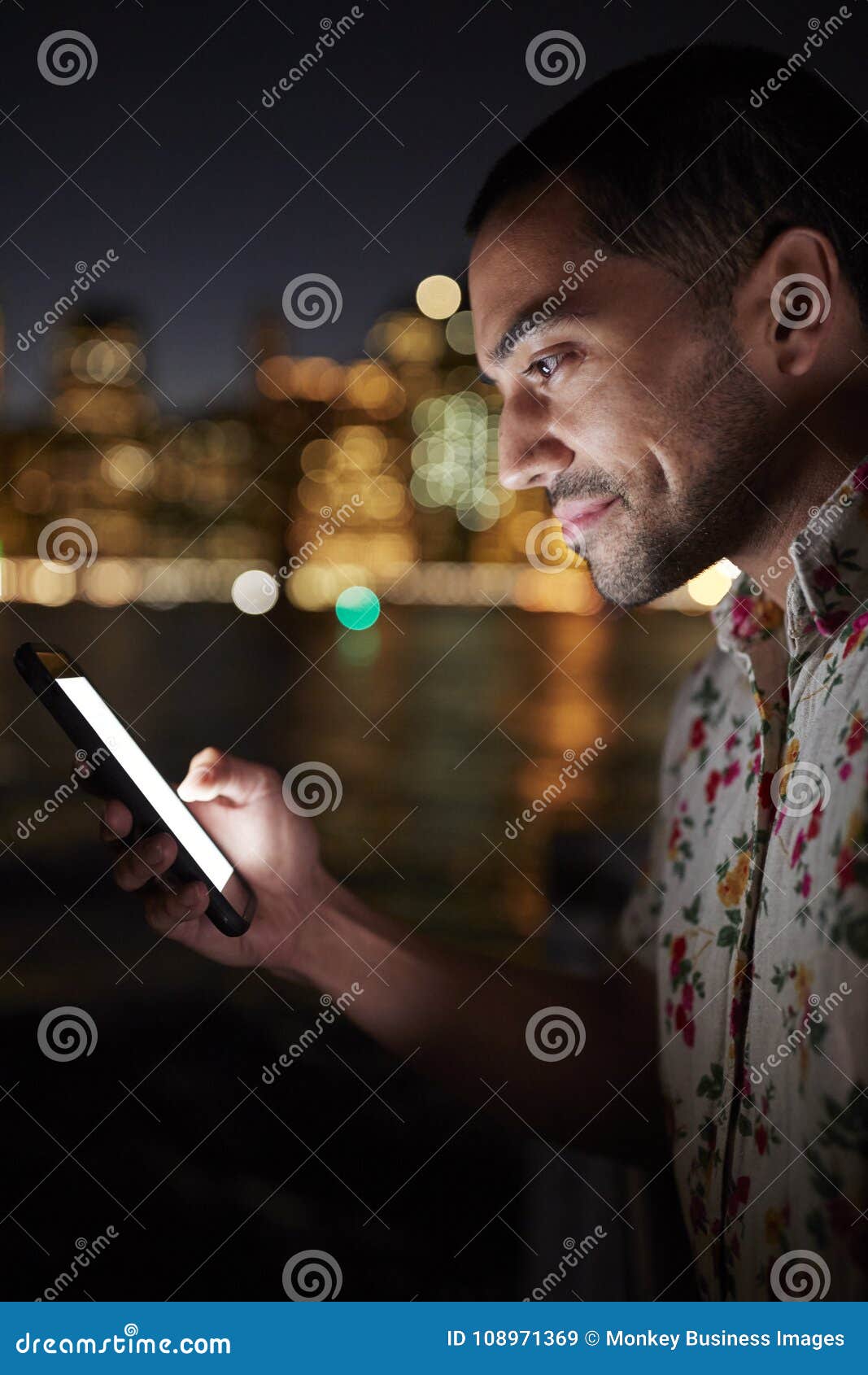 Man Using Mobile Phone At Night With City Skyline In