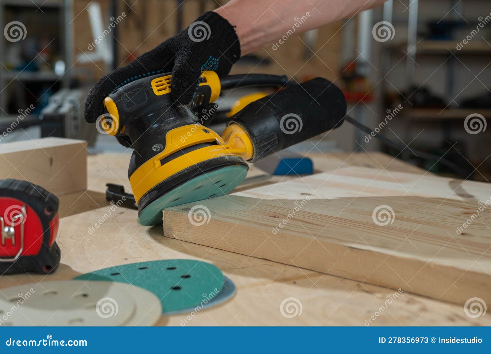 a man using an orbital wood sander in a workshop. close-up of a carpenter& x27;s hands.