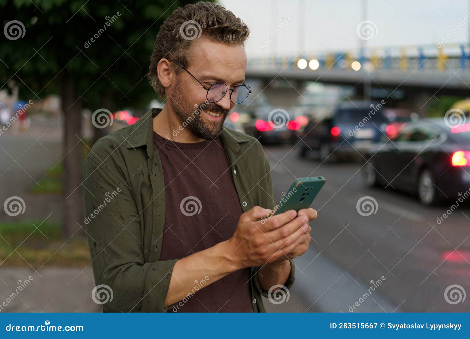 man using phone on evening city street, presumably to call taxi cab driver. soft evening lighting adds touch of ambiance