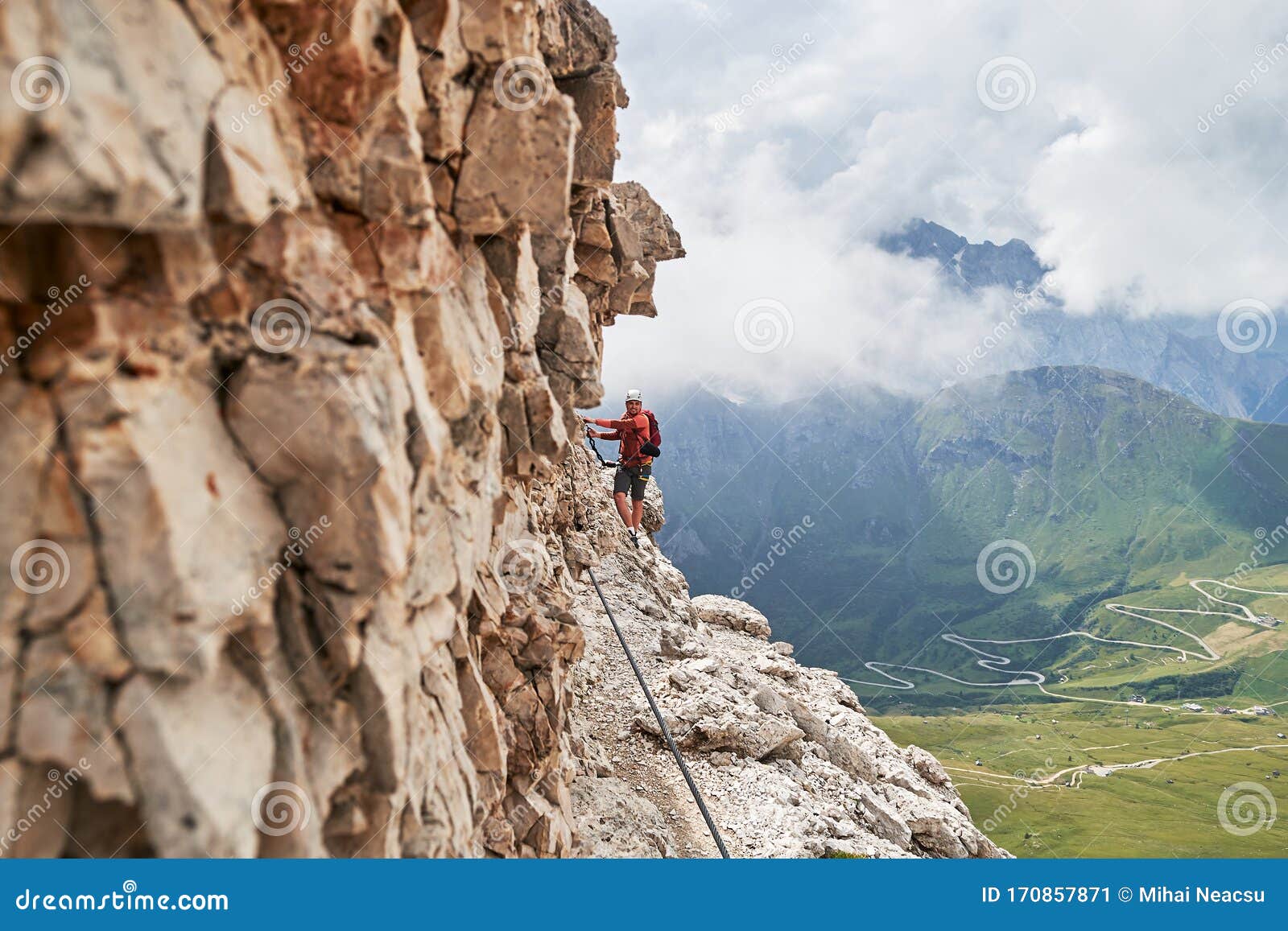 man on via ferrata cesare piazzetta, dolomites mountains, italy, close to the rock wall, with a winding road below, in summer