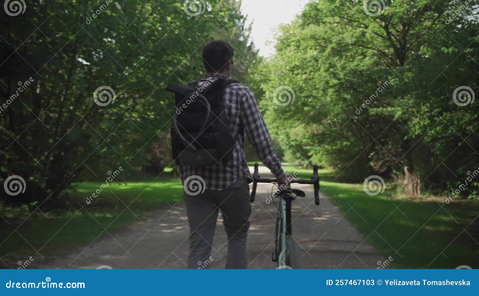 Man Walks Next To Bicycle with Backpack on Which Hangs Cycle Lock. Back