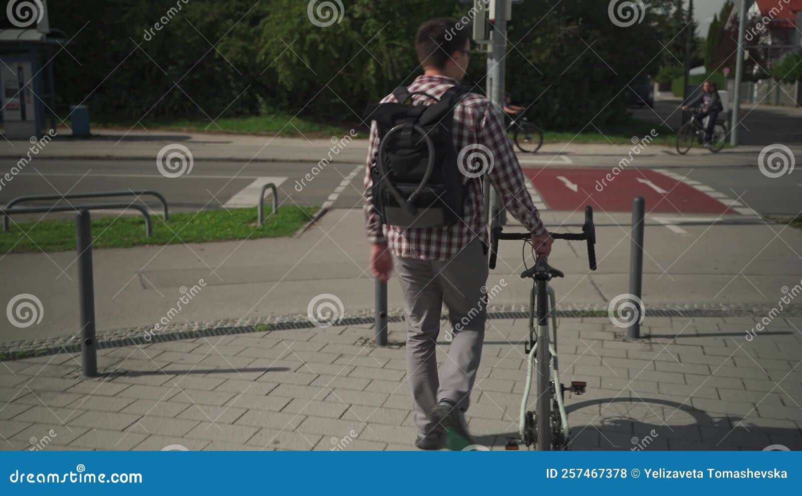 Man Walks Next To Bicycle with Backpack on Which Hangs Cycle Lock. Back