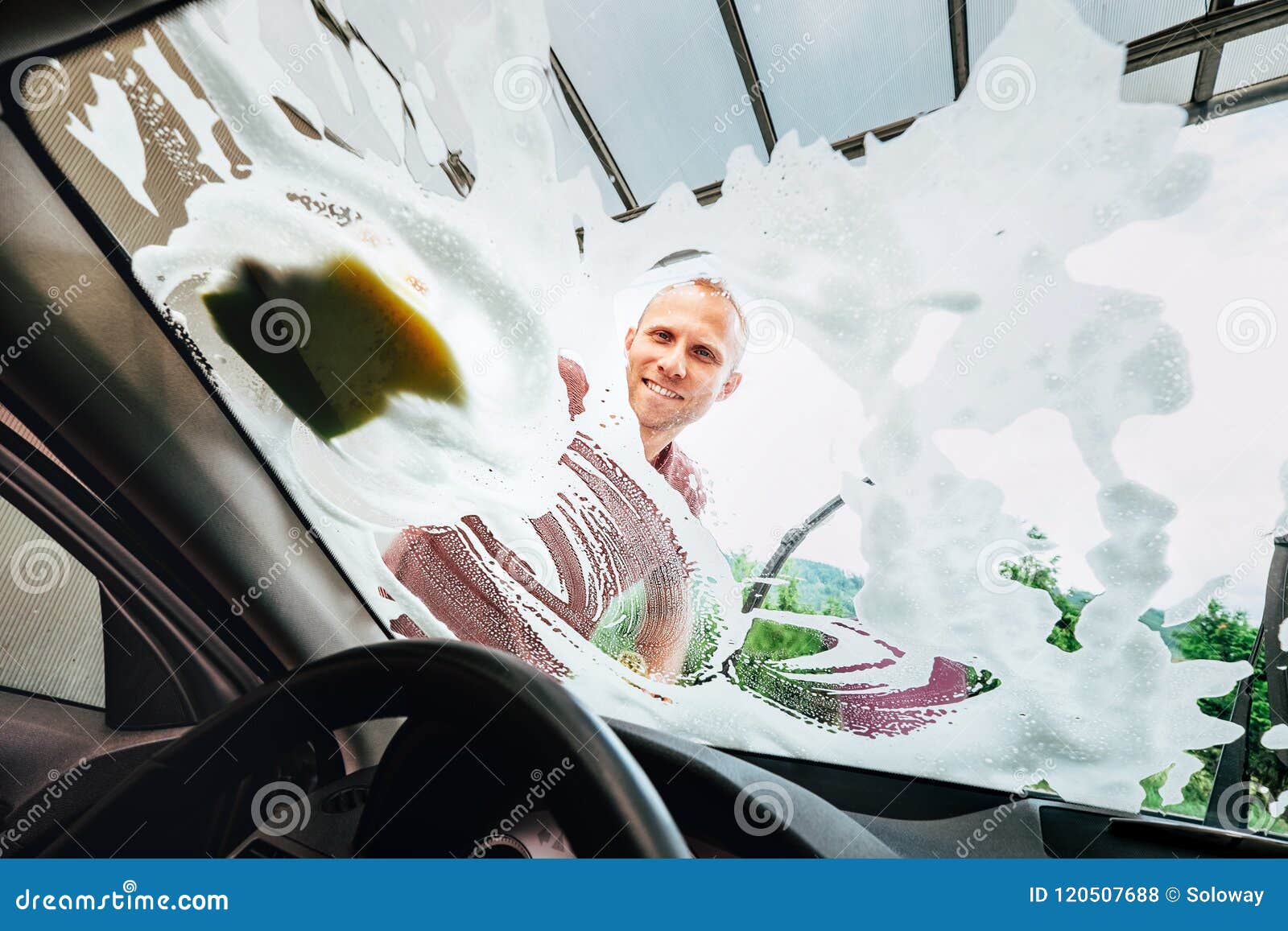 man washes car front windows with soap foam
