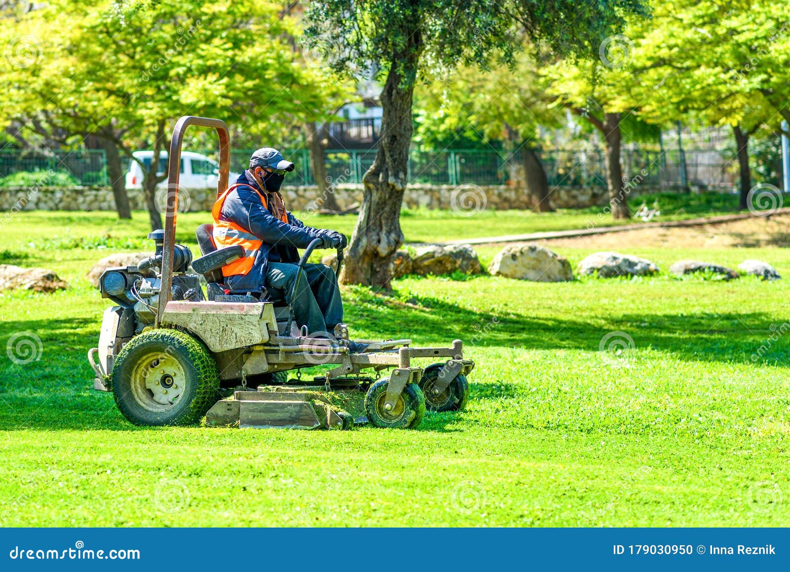 Man Wearing Black Face Mask Mows the Grass with Lawn Mower. Mow
