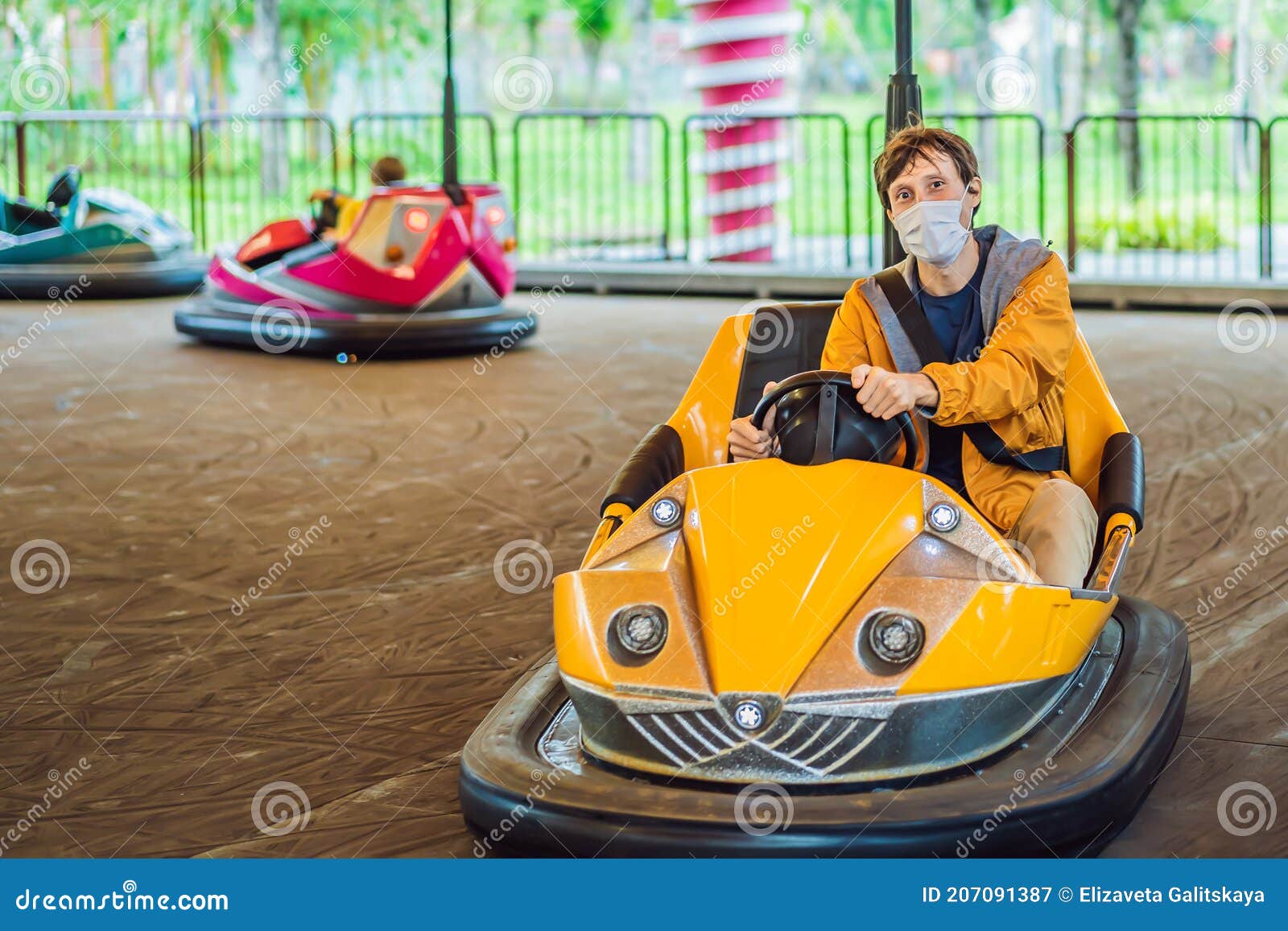 man wearing a medical mask during covid-19 coronavirus having a ride in the bumper car at the amusement park